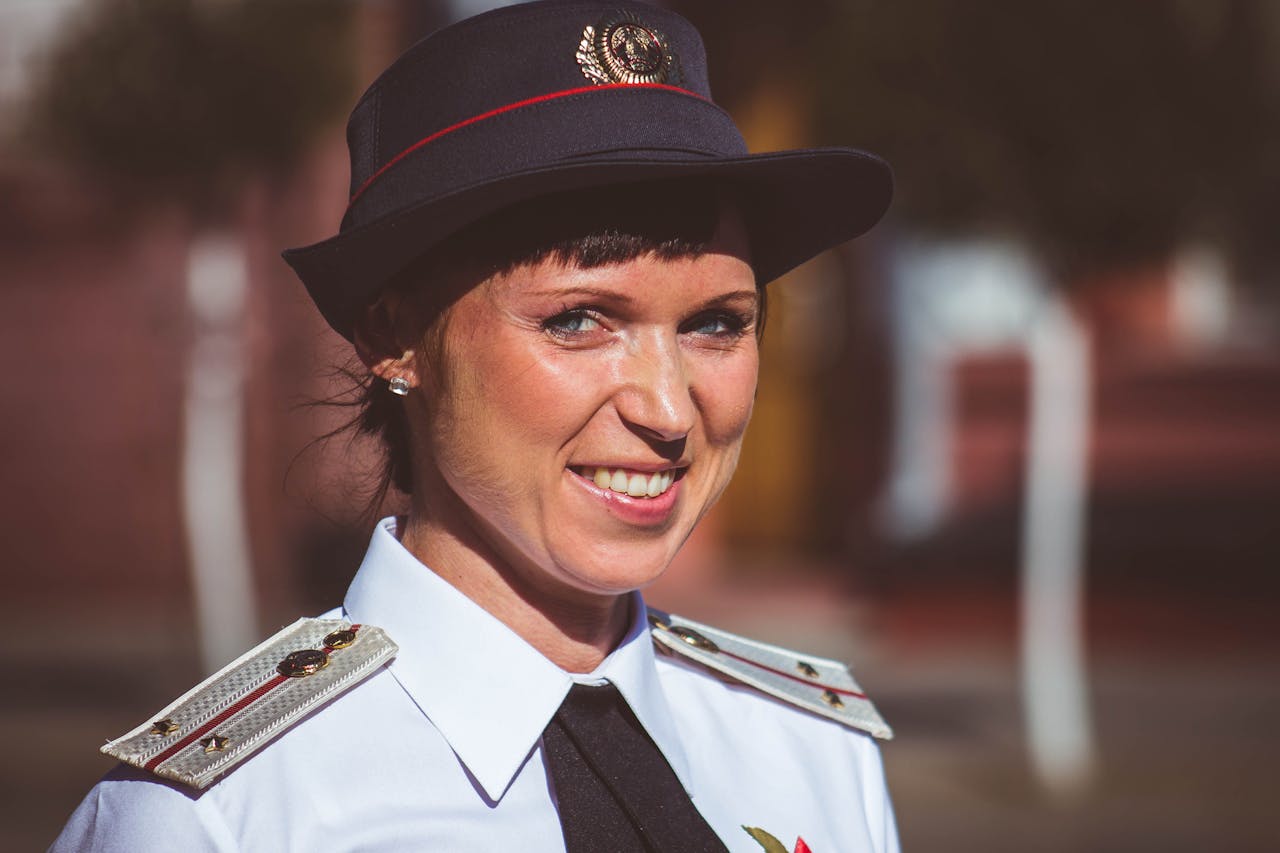 Portrait of a smiling female officer outdoors, wearing a uniform and hat in daylight.